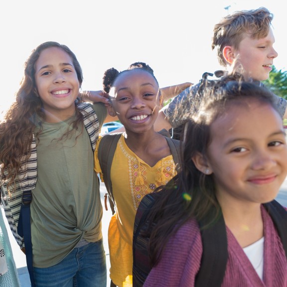 A group of young school children outside with their backpacks on