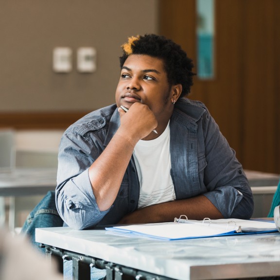 student sits thoughtfully at a desk