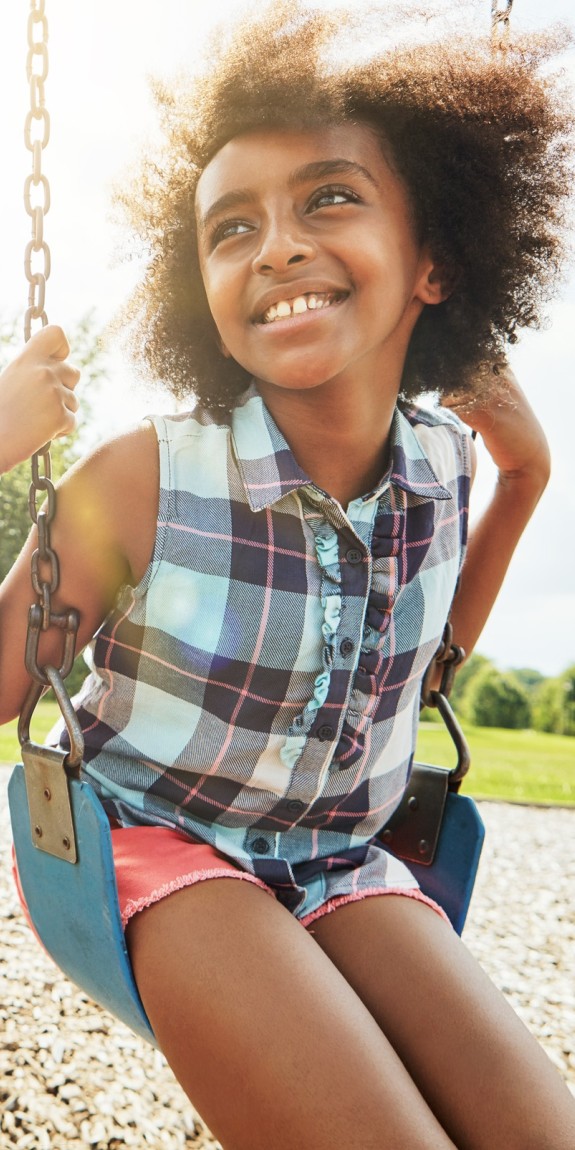 Happy looking child on a swing. The sun is shining behind their head